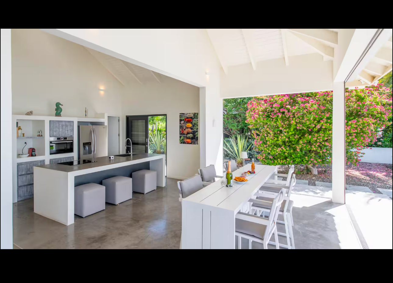 Covered dining space and open kitchen beside bougainvillea